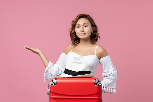 Vista frontal de la mujer joven preparándose para las vacaciones con bolsa y posando en la pared rosa