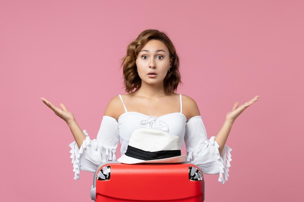 Vista frontal de la mujer joven preparándose para las vacaciones con bolsa roja en la pared rosa