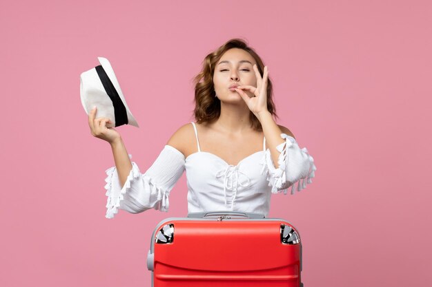 Vista frontal de la mujer joven preparándose para las vacaciones con bolsa roja y posando en el modelo de piso rosa color viaje de viaje de vacaciones al mar