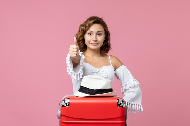 Vista frontal de la mujer joven preparándose para las vacaciones con bolsa roja posando en la pared rosa