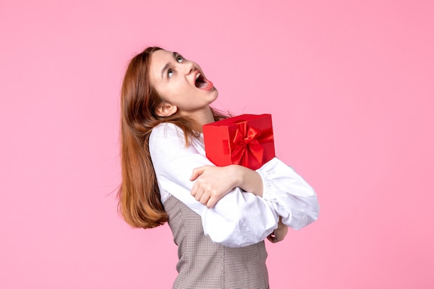 Vista frontal mujer joven con presente en paquete rojo sobre fondo rosa amor fecha marzo horizontal sensual igualdad mujer