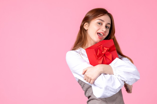 Vista frontal mujer joven con presente en paquete rojo sobre fondo rosa fecha de amor marcha sensual igualdad mujer
