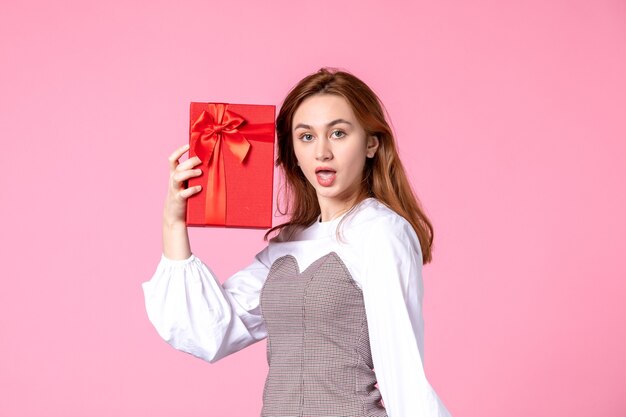 Vista frontal mujer joven con presente en paquete rojo sobre fondo rosa fecha de amor marzo horizontal igualdad sensual mujer dinero