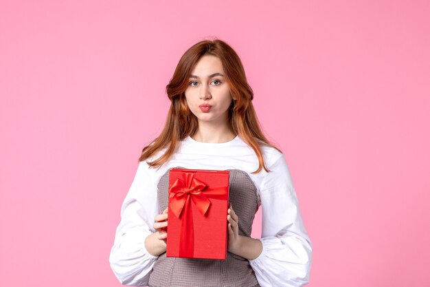 Vista frontal mujer joven con presente en paquete rojo sobre fondo rosa fecha de amor marzo horizontal regalo sensual perfume mujer fotos dinero igualdad