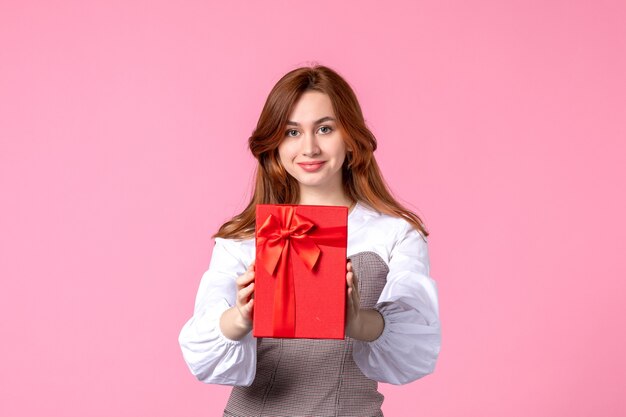 Vista frontal mujer joven con presente en paquete rojo sobre fondo rosa fecha de amor marzo regalo horizontal perfume igualdad mujer foto dinero