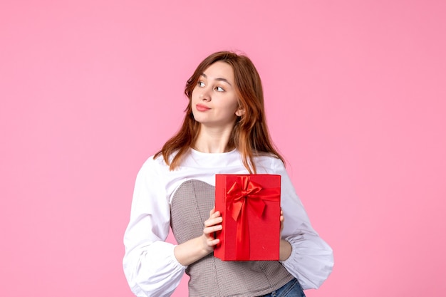 Vista frontal mujer joven con presente en paquete rojo sobre fondo rosa fecha de amor marzo regalo horizontal perfume mujer foto dinero igualdad