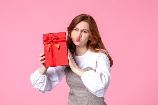 Vista frontal mujer joven con presente en paquete rojo sobre fondo rosa fecha de amor marzo regalos sensuales horizontales perfume igualdad mujer foto dinero