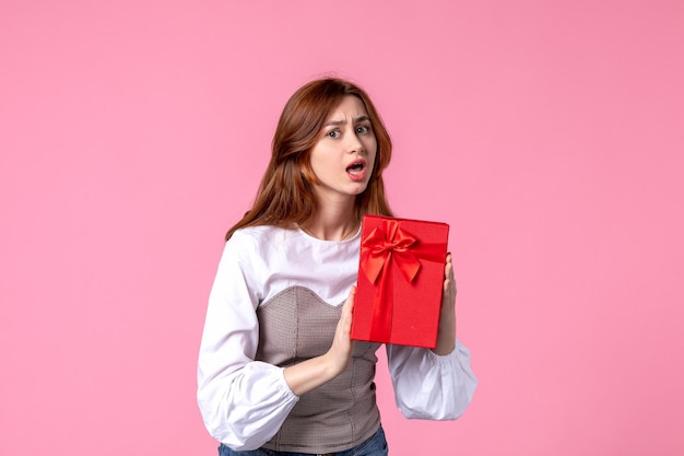 Vista frontal mujer joven con presente en paquete rojo sobre fondo rosa marzo dinero horizontal sensual igualdad mujer regalos