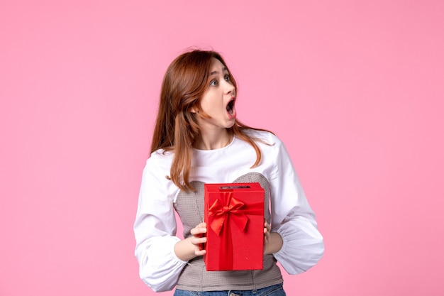 Vista frontal mujer joven con presente en paquete rojo sobre fondo rosa marzo horizontal sensual regalo perfume foto dinero igualdad