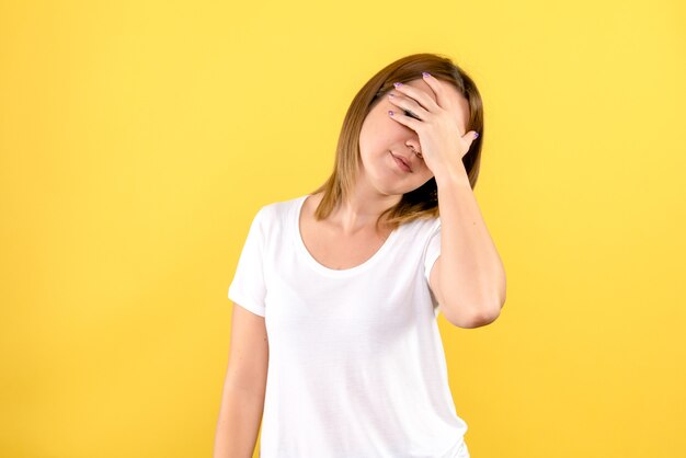 Vista frontal de la mujer joven que cubre su rostro en la pared amarilla