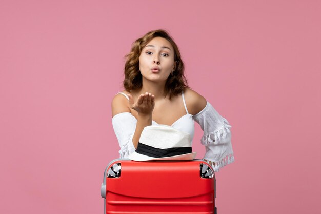 Vista frontal de la mujer joven que se prepara para las vacaciones enviando besos al aire en la pared rosa