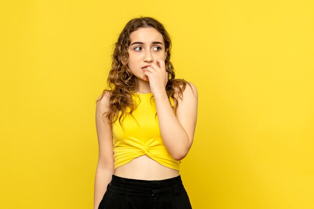 Vista frontal de la mujer joven que se siente asustada en la pared amarilla