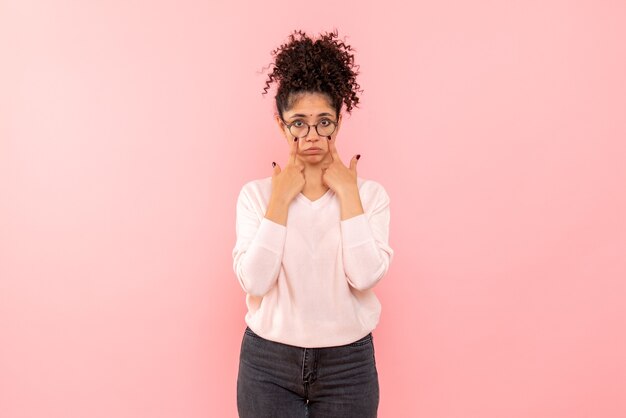 Vista frontal de la mujer joven que se siente triste en la pared rosa