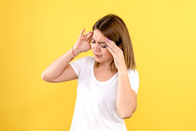 Vista frontal de la mujer joven que tiene dolor de cabeza en la pared amarilla