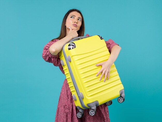 Vista frontal de la mujer joven que va de vacaciones y que sostiene la bolsa grande pensando en el fondo azul viaje mar vacaciones viaje mujer en el extranjero