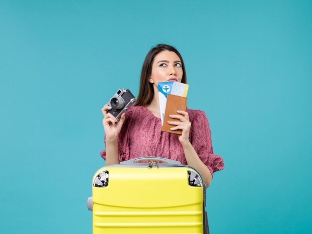Vista frontal mujer joven que va de vacaciones sosteniendo la cámara y boletos sobre fondo azul claro viaje vacaciones mujer mar en el extranjero