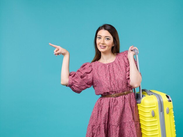 Vista frontal de la mujer joven que va de vacaciones con su bolsa amarilla sobre el fondo azul verano mujer viaje viaje humano mar