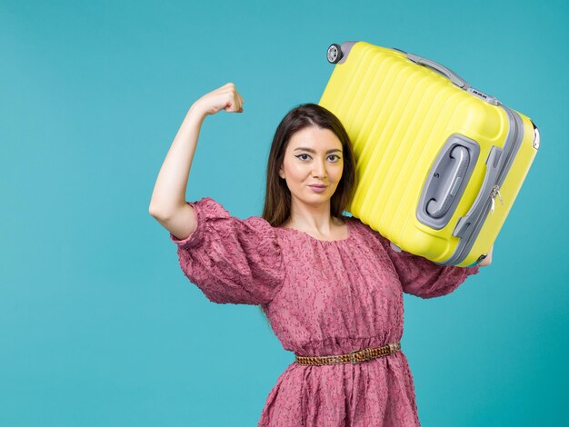 Vista frontal de la mujer joven que va de vacaciones con su bolsa amarilla sobre fondo azul viaje de verano mujer humana mar