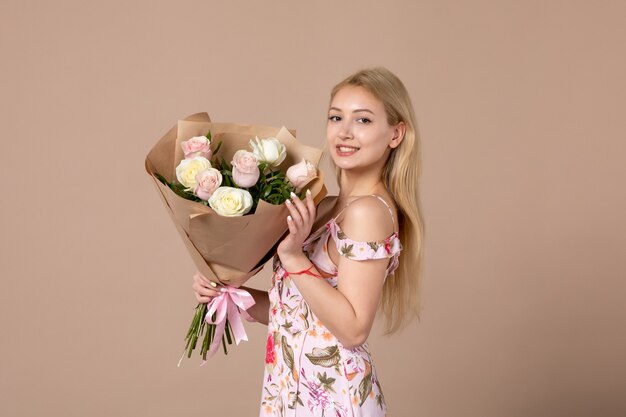 Vista frontal de la mujer joven con ramo de rosas hermosas en la pared marrón