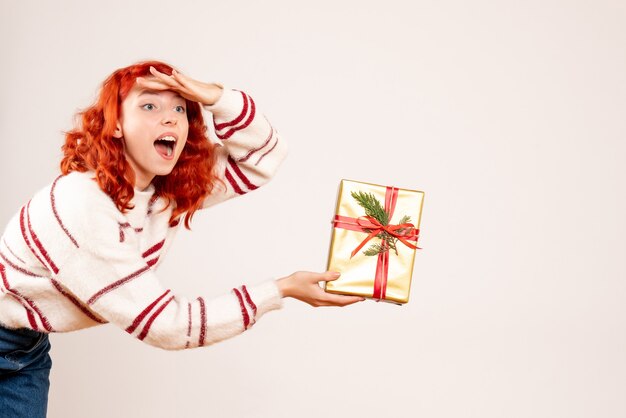 Vista frontal de la mujer joven con regalo de Navidad en la pared blanca