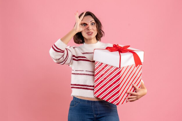 Vista frontal de la mujer joven con regalo de Navidad en la pared rosa