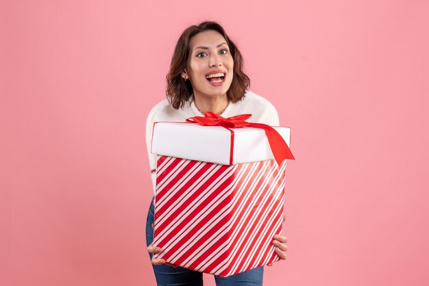 Vista frontal de la mujer joven con regalo de Navidad en la pared rosa