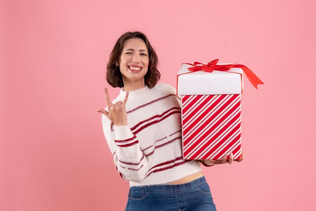 Vista frontal de la mujer joven con regalo de Navidad en la pared rosa