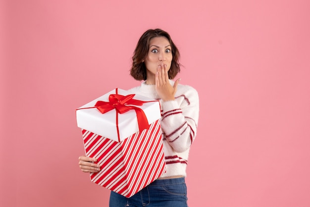 Vista frontal de la mujer joven con regalo de Navidad en la pared rosa