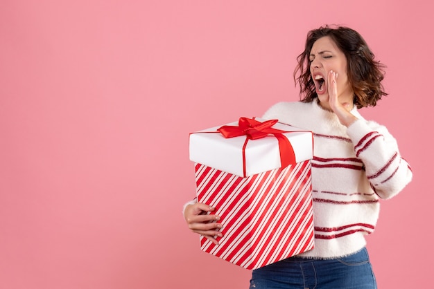 Vista frontal de la mujer joven con regalo de Navidad en la pared rosa