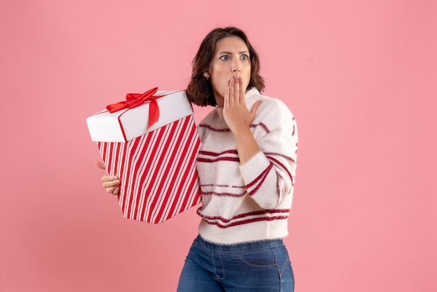 Vista frontal de la mujer joven con regalo de Navidad sorprendido en la pared rosa