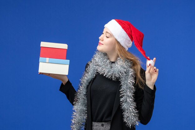 Vista frontal de la mujer joven con regalos de año nuevo en la pared azul