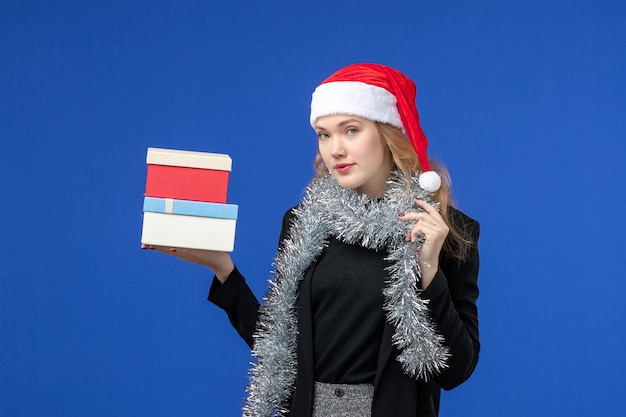 Vista frontal de la mujer joven con regalos de año nuevo en la pared azul