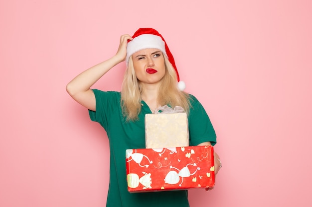 Vista frontal de la mujer joven con regalos de Navidad confundidos en la pared rosa