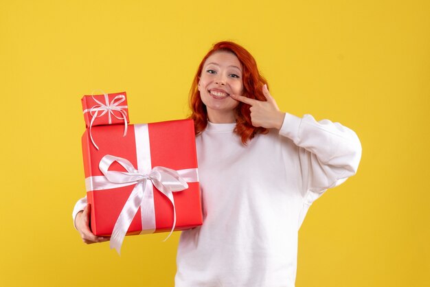 Vista frontal de la mujer joven con regalos de Navidad en la pared amarilla