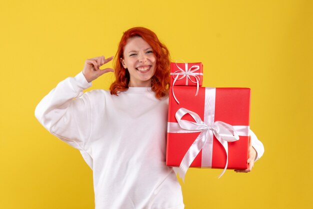 Vista frontal de la mujer joven con regalos de Navidad en la pared amarilla