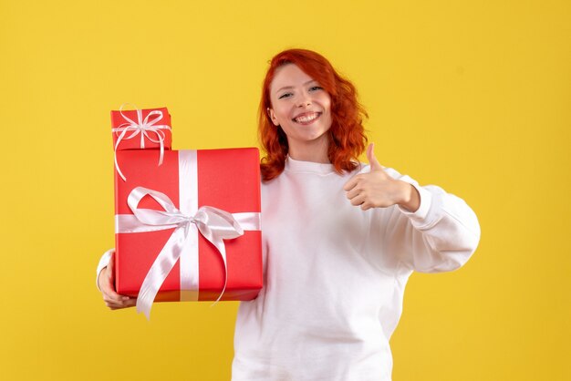 Vista frontal de la mujer joven con regalos de Navidad en la pared amarilla