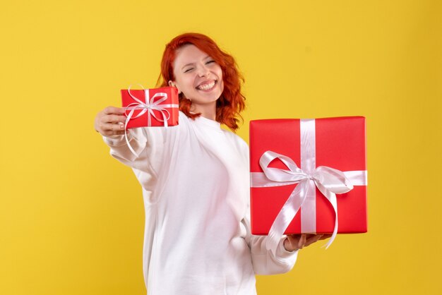 Vista frontal de la mujer joven con regalos de Navidad en la pared amarilla