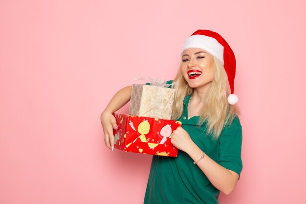 Vista frontal de la mujer joven con regalos de Navidad en la pared rosa