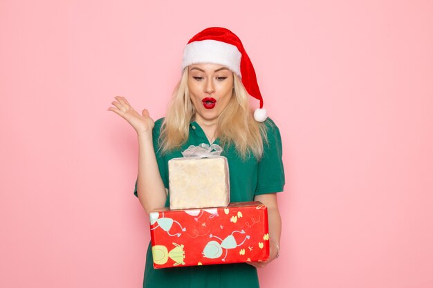 Vista frontal de la mujer joven con regalos de Navidad en la pared rosa