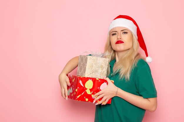 Vista frontal de la mujer joven con regalos de Navidad en la pared rosa