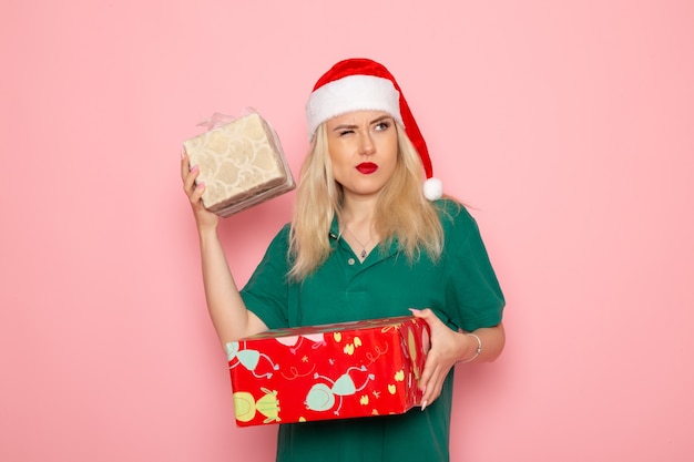 Vista frontal de la mujer joven con regalos de Navidad en la pared rosa