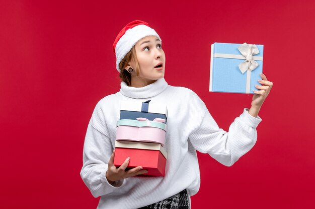 Vista frontal mujer joven con regalos navideños sobre fondo rojo.