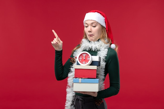 Vista frontal mujer joven con regalos con reloj sobre fondo rojo.