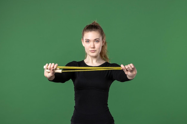 Foto gratuita vista frontal mujer joven en ropa deportiva negra sosteniendo saltar la cuerda sobre fondo verde deporte atleta yoga salud color del cuerpo