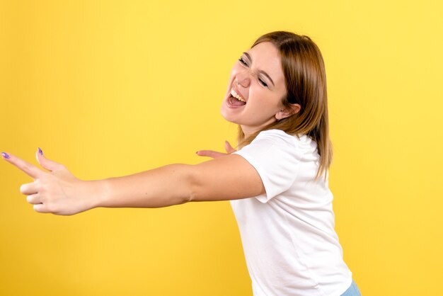 Vista frontal de una mujer joven con rostro emocional en la pared amarilla