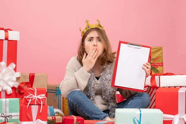 Vista frontal mujer joven sentada alrededor de regalos con nota en sus manos