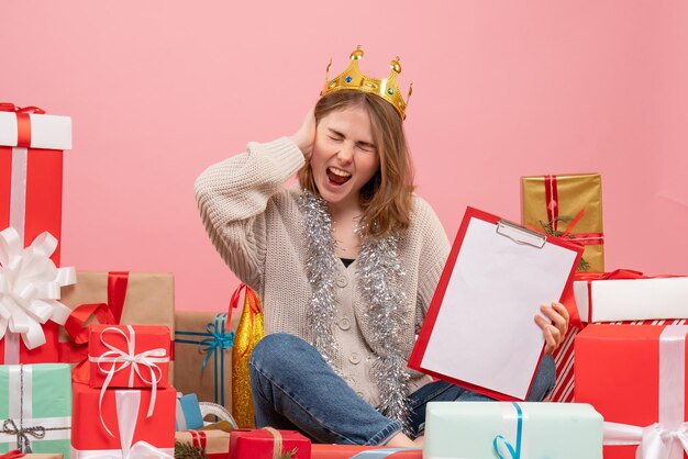 Vista frontal mujer joven sentada alrededor de regalos con nota en sus manos