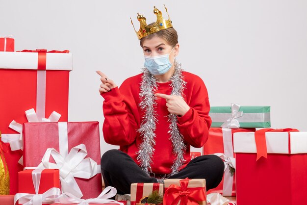 Vista frontal mujer joven sentada con regalos de Navidad en máscara y corona