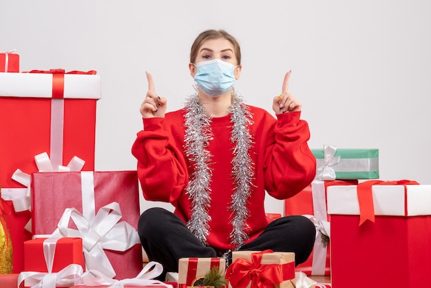 Vista frontal mujer joven sentada con regalos de Navidad en máscara estéril