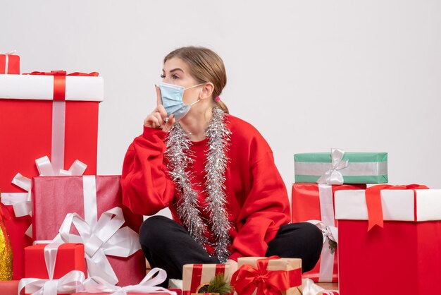 Vista frontal mujer joven sentada con regalos de Navidad en máscara estéril